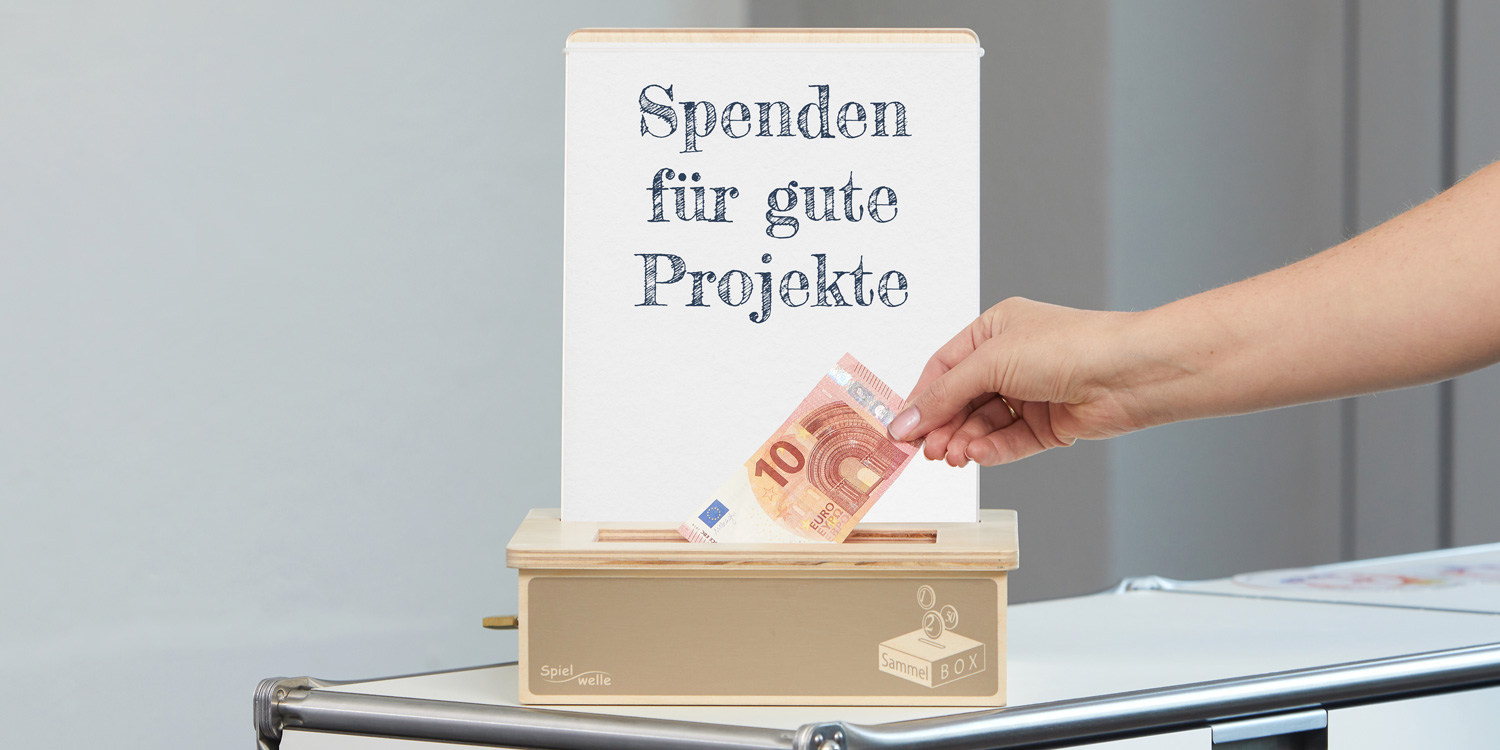 Eine Hand steckt einen Zehn-Euro-Schein in die Spielwelle SammelBOX. Im Hintergrund steht der Text Spenden für gute Projekte.